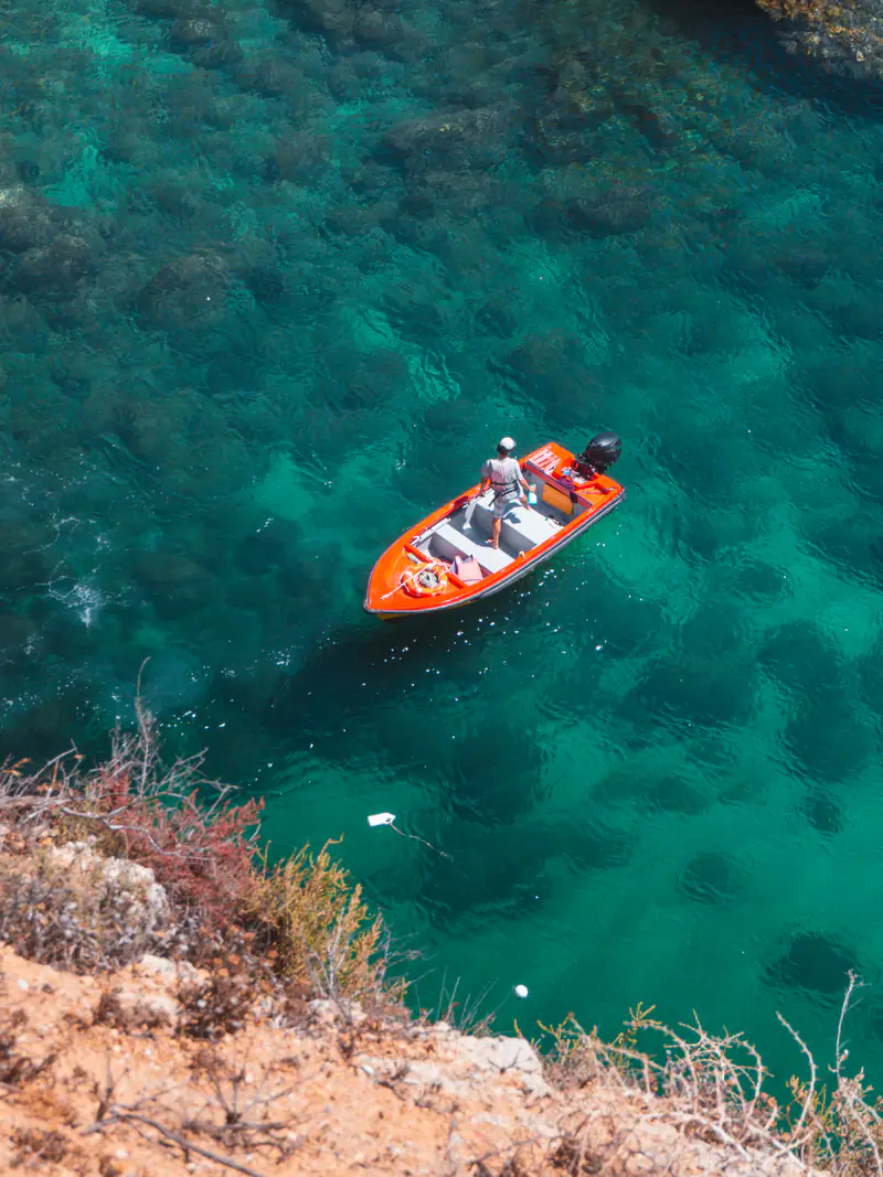 Barca rossa nell'acqua turchese sotto la scogliera