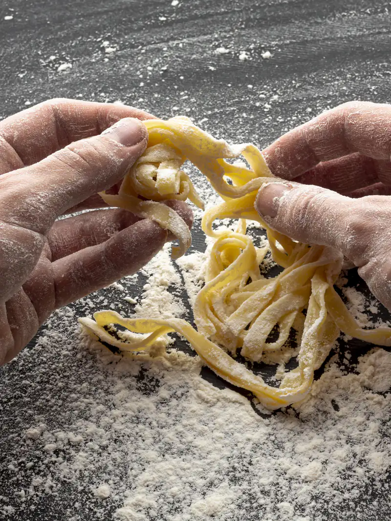 Mani che lavorano la pasta fresca sulla farina