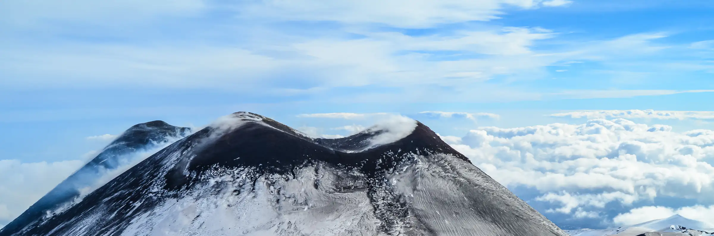 La vetta dell'Etna innevata, col suo pennacchio di fumo sopra un mare di nuvole